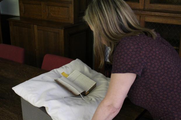 A woman with shoulder length brown hair looks at an old book on a book stand in the library